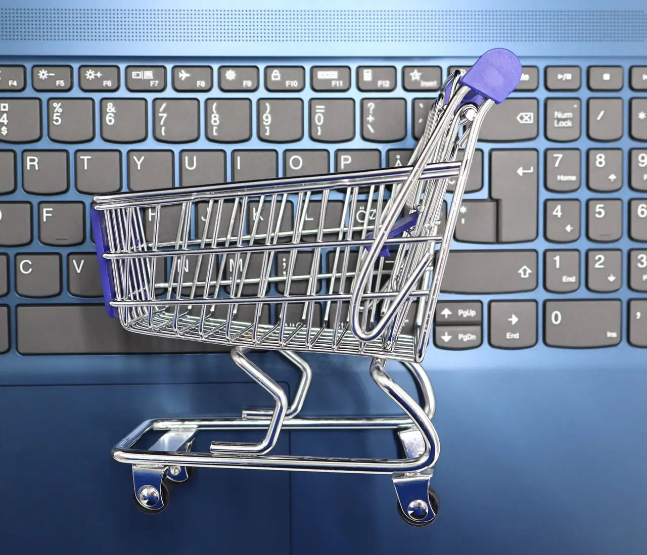 services-03 A miniature shopping cart placed on a laptop keyboard symbolizing online shopping and e-commerce.