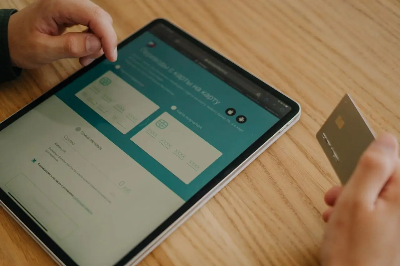 gallery-1 Hands making an online purchase using a tablet and credit card on a wooden table.