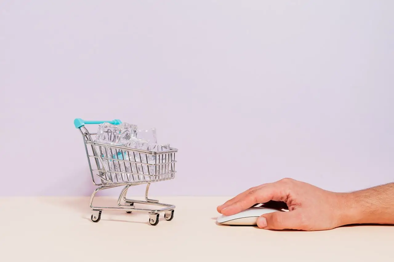 hero-img-02 Conceptual image of a hand on a mouse next to a miniature shopping cart filled with ice cubes, symbolizing online shopping.