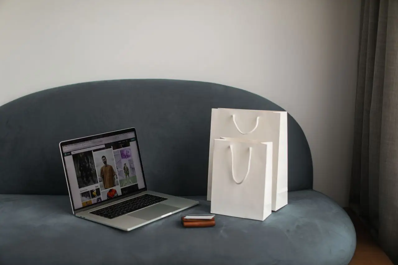 services-02 Online shopping setup with a laptop and shopping bags on a stylish couch.