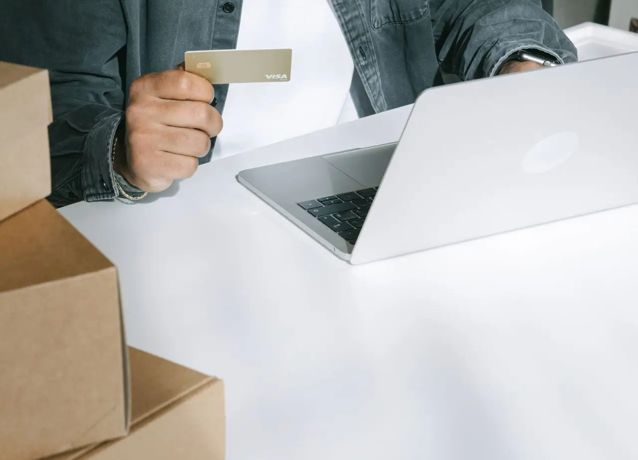 about-01 Person using a credit card for online shopping on a laptop surrounded by shipping boxes.
