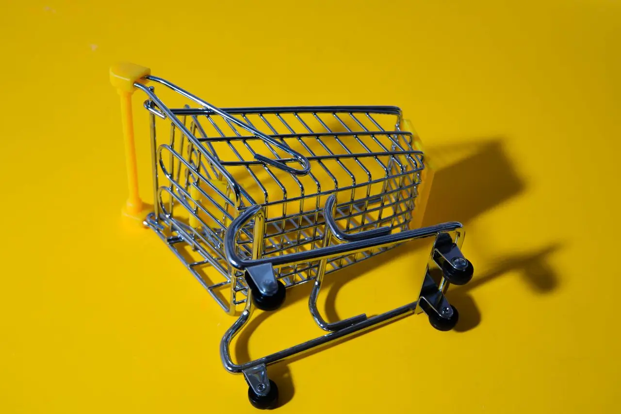 services-01 Close-up of a toy shopping cart on a vivid yellow surface, casting shadows.