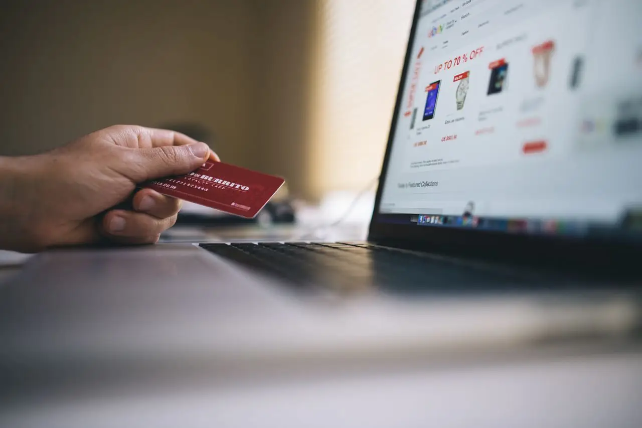 hero-img-01 Person holding a credit card while shopping online on a laptop, indicating ecommerce transactions.
