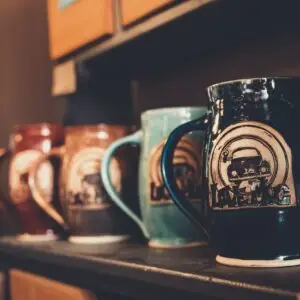 A collection of artistic ceramic mugs with retro designs displayed on a wooden shelf.